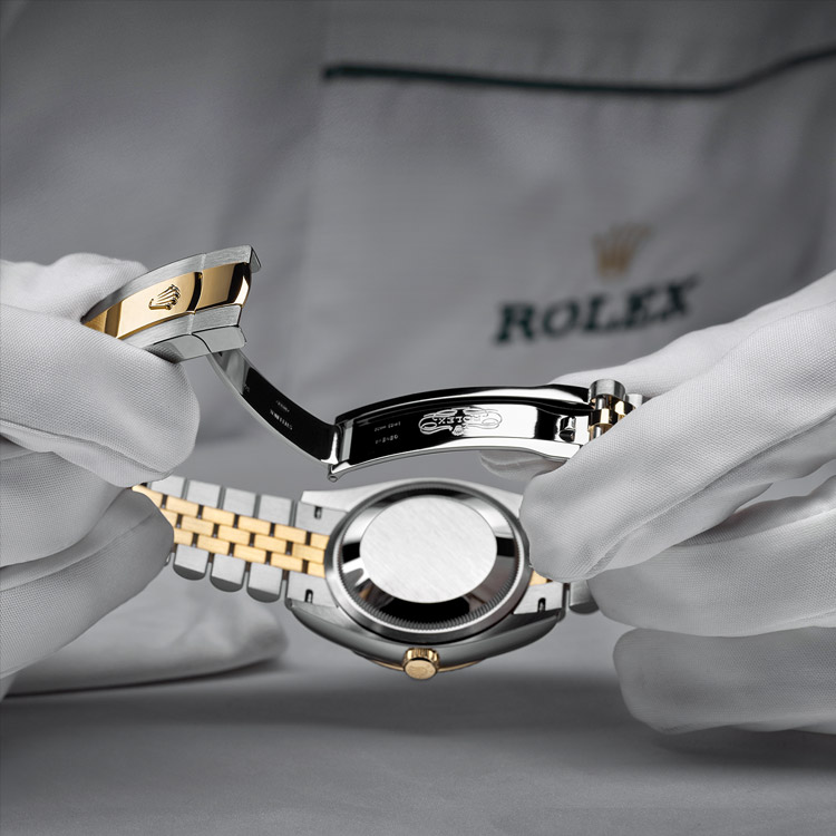 Eine Person mit Handschuhen öffnet das Faltschließen-Armband einer Rolex Uhr 