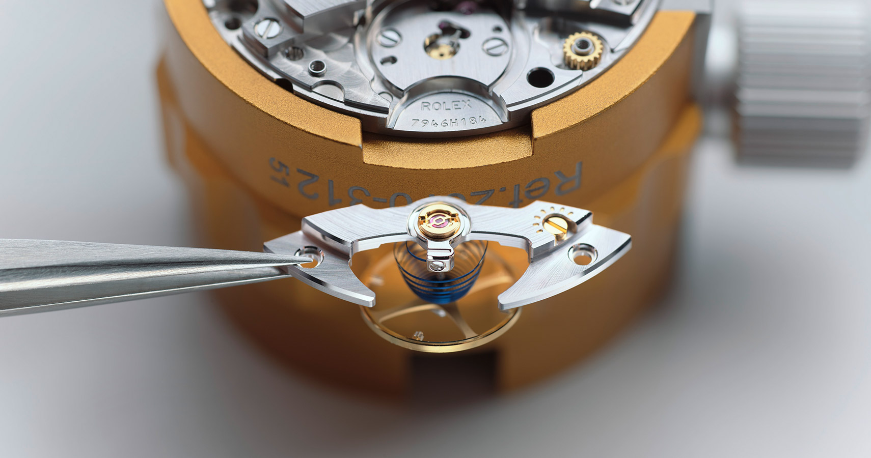 Von dem Werk einer Rolex Uhr wird ein Teil mit einer Pinzette vorsichtig herausgenommen